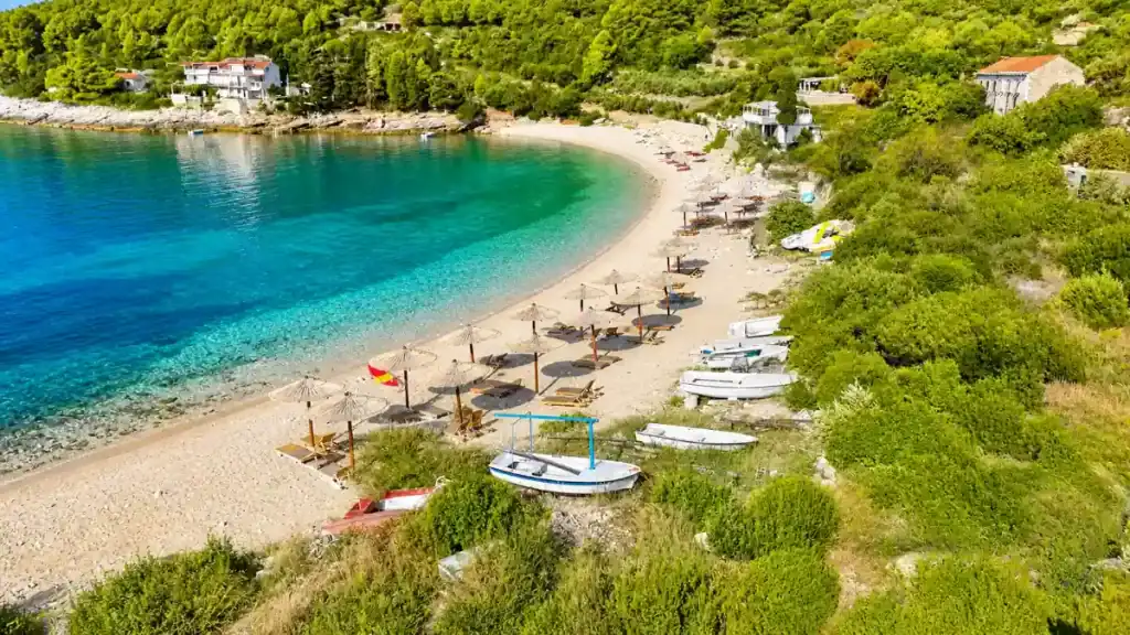 Straw umbrellas lining the curved pebble shoreline at Pupnatska Luka cove