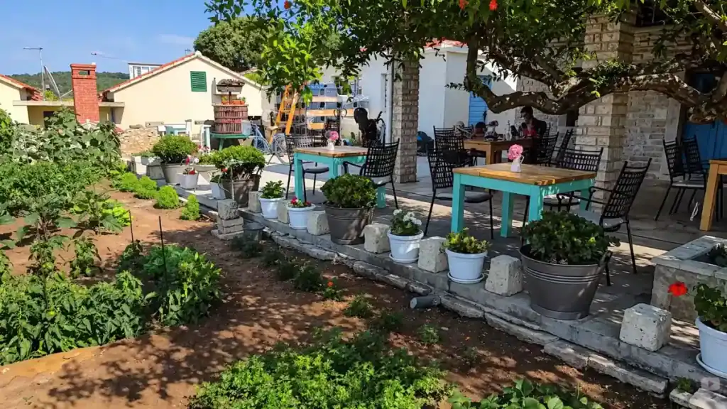 Outdoor garden terrace at Vitis Winery in Lumbarda with potted flowers, vegetable beds, and guests dining during a Korčula Town winery day