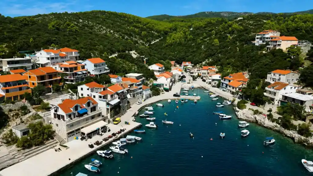 Aerial shot of Zavalatica harbour filled with boats, a quieter alternative during Korčula Town's busy times, forested hills behind