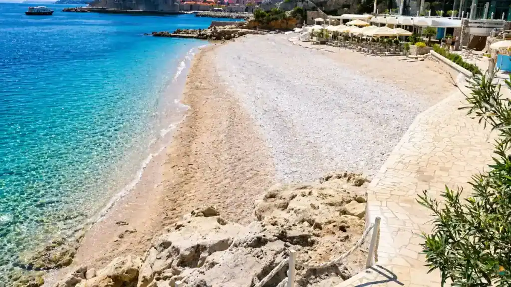 Banje Beach curved shoreline with sunbeds, parasols, and old town walls visible, among the most popular Korčula Town swim spots