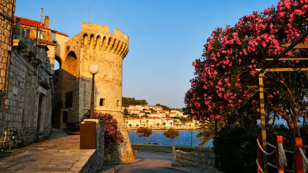 Medieval defensive tower at the edge of Korčula old town walls framed by flowering oleander at golden hour