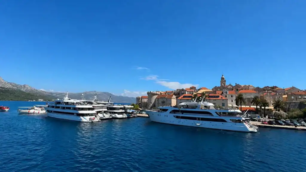 Large cruise vessels moored in a harbour with a walled medieval town rising behind
