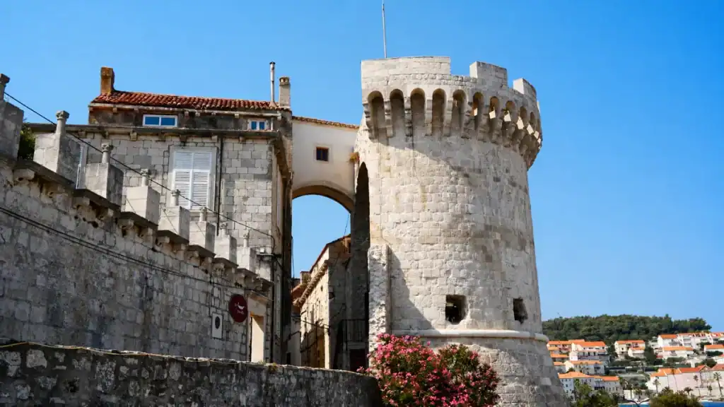 Kanavelić Tower and stone archway gateway rising above Korčula old town walls, pink oleander in the foreground