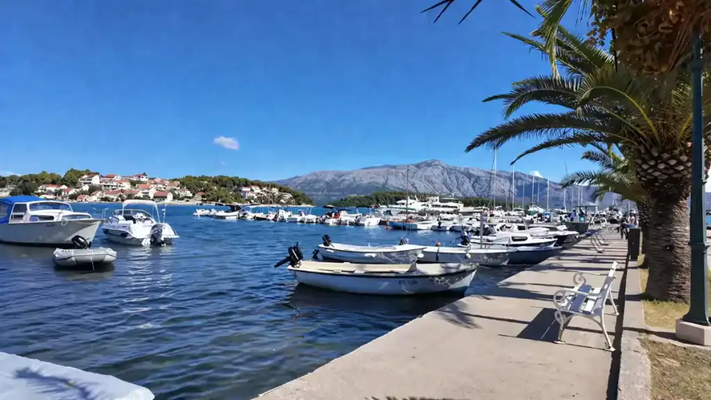 Small boats moored along Lumbarda harbour promenade with mountains in the background