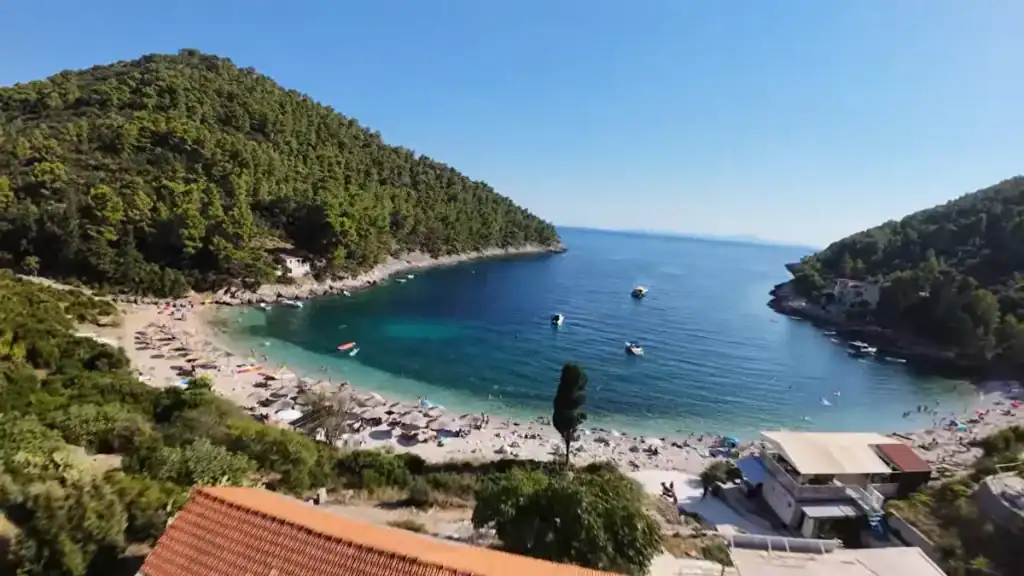 Aerial shot of Pupnatska Luka's curved pebble beach tucked between pine-covered hills with turquoise water below
