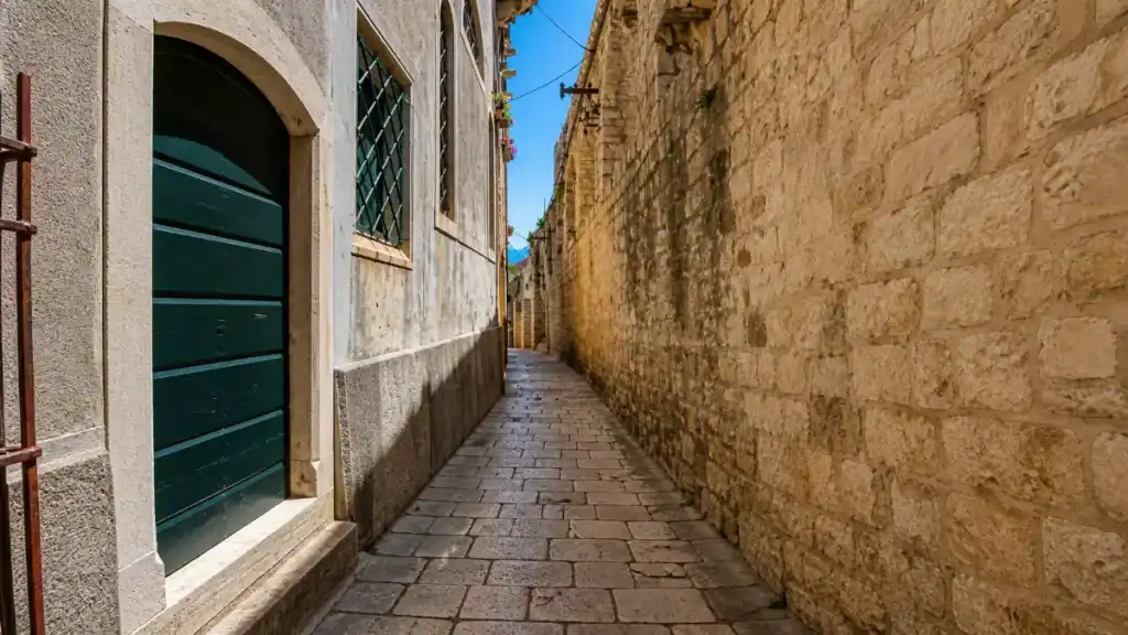 Narrow cobblestone lane flanked by tall limestone walls inside Korčula old town on a sunny day