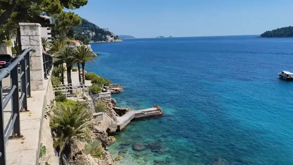 Coastal path with palm trees and stone steps leading down to a narrow jetty above deep blue water near Korčula old town