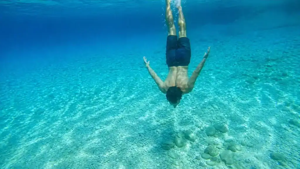 Man diving underwater toward a pale pebble seabed in crystal-clear Adriatic water off Korčula island