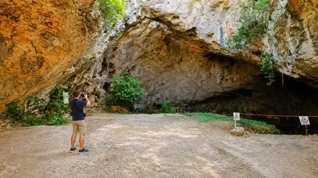 Visitor photographing the wide rock entrance to Vela Spila cave above Vela Luka