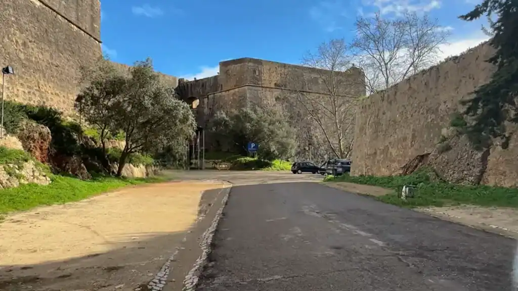 Narrow road running between ancient stone fortress walls with parking area in Setúbal