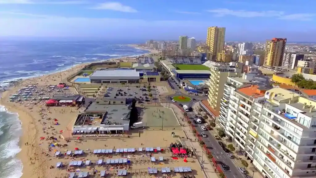 Packed beach lined with sunbeds beside a dense urban seafront with high-rise buildings