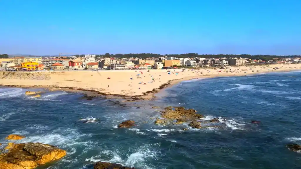 Rocky Atlantic shoreline with a wide sandy beach and Vila do Conde town behind