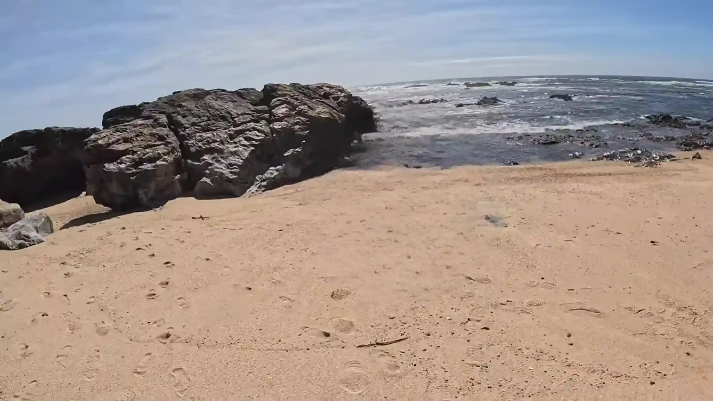 Large rock formation on Vila do Conde beach with waves breaking beyond