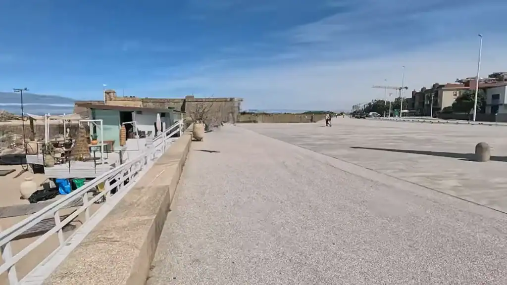 Wide coastal promenade beside a stone fort wall with a beach bar terrace
