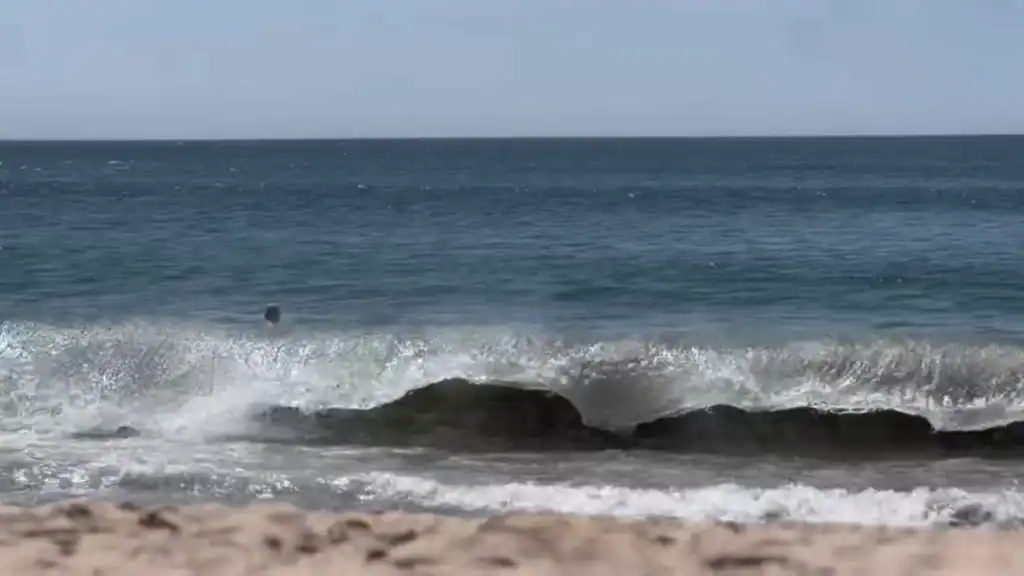 Atlantic waves crashing over dark rocks at Vila do Conde beach with a swimmer beyond the break