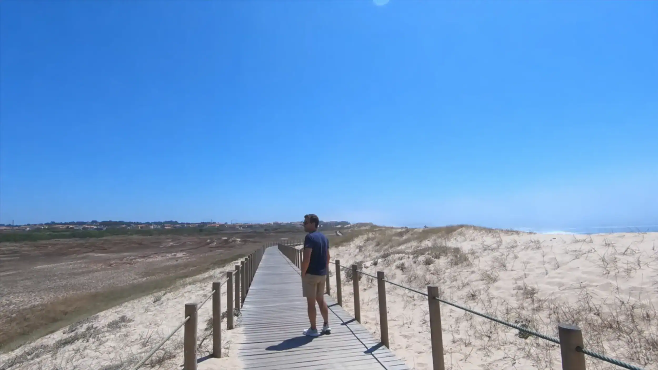 Man standing on a wooden boardwalk through sand dunes on the Vila do Conde coastal walk