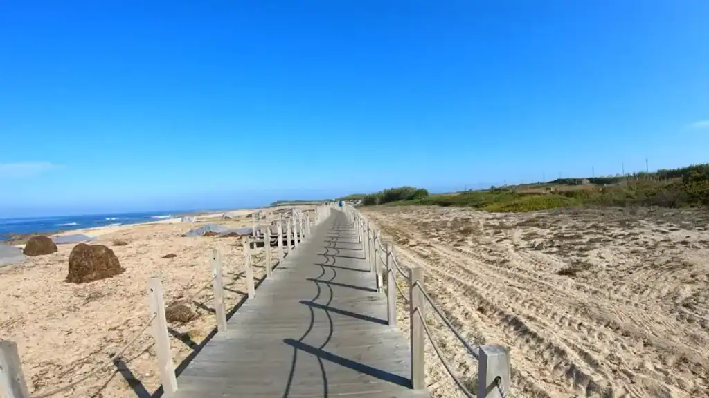 Straight timber boardwalk running beside an open Atlantic beach with a lone walker ahead