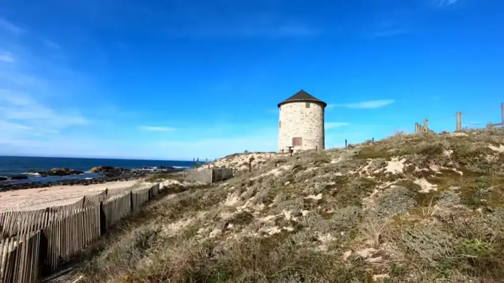 Round stone windmill on coastal dunes above a sandy Atlantic beach