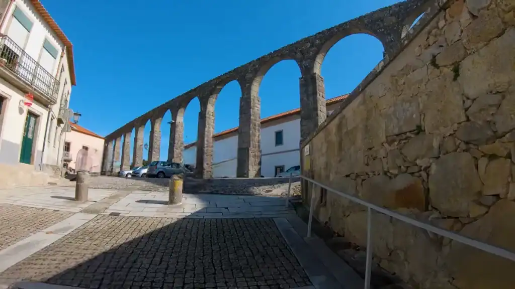 Stone arches of a historic aqueduct rising above a cobbled town street
