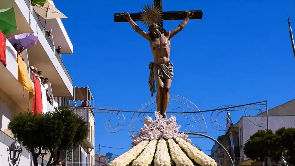 Tall crucifixion statue mounted on a white flower-covered float against a deep blue sky