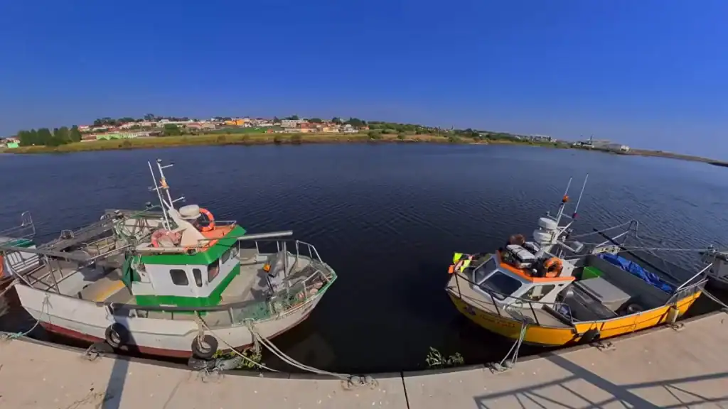 Two small fishing boats moored at a concrete quay on a calm river estuary