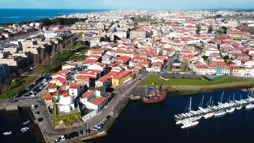 Vila do Conde harbour with sailboats, a tall ship, and terracotta rooftops stretching to the coast