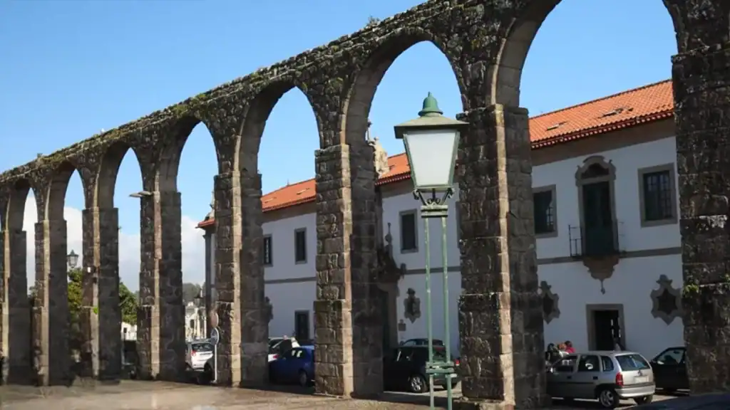 Moss-covered stone aqueduct arches running alongside a whitewashed convent building