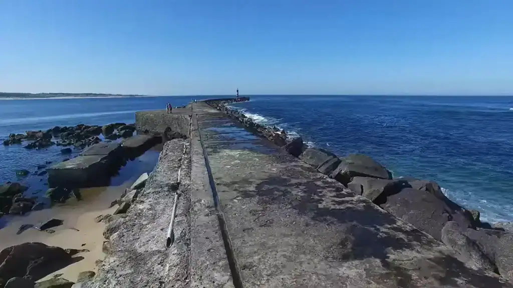 Long stone jetty stretching into deep blue ocean with a small lighthouse at the end