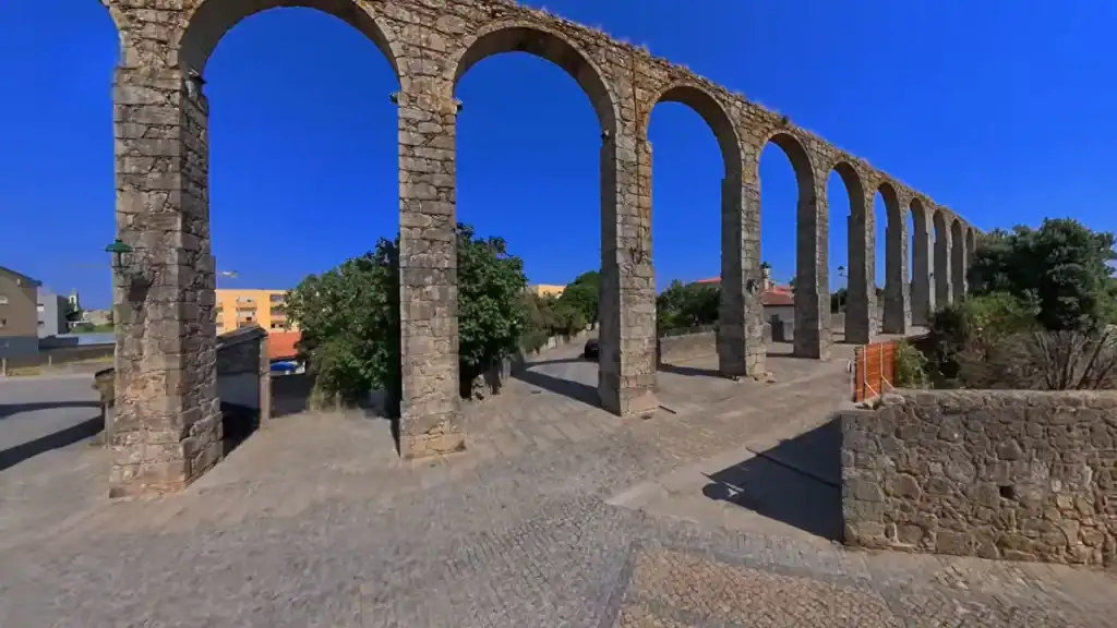 Stone arched aqueduct stretching along a cobbled street under a deep blue sky