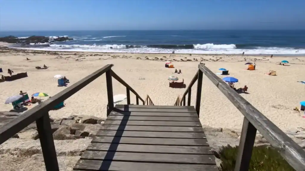 Wooden steps descending onto a sandy beach dotted with colourful parasols and Atlantic breakers beyond