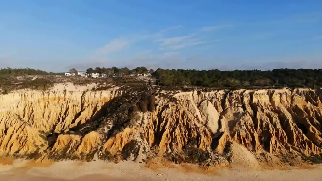 Deeply eroded sandstone cliffs with orange and ochre ridges above a sandy beach