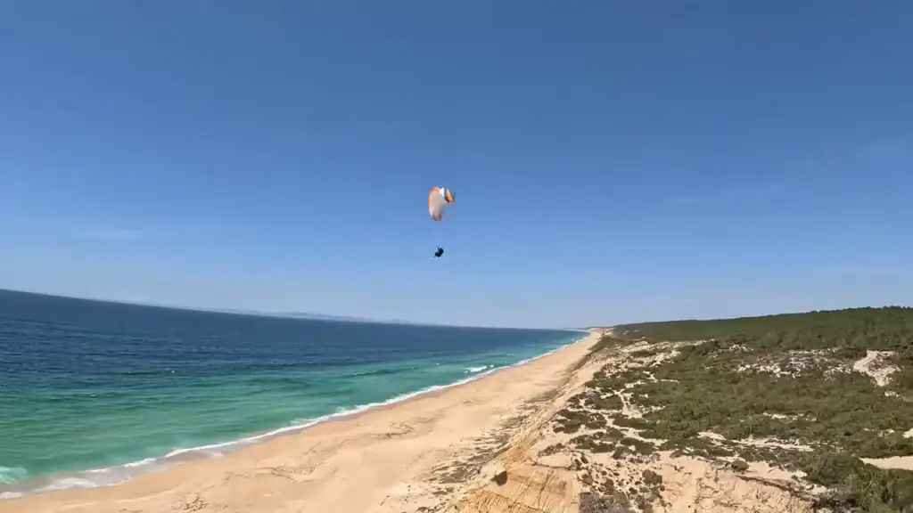 Paraglider soaring over Aberta Nova beach with turquoise Atlantic waters below
