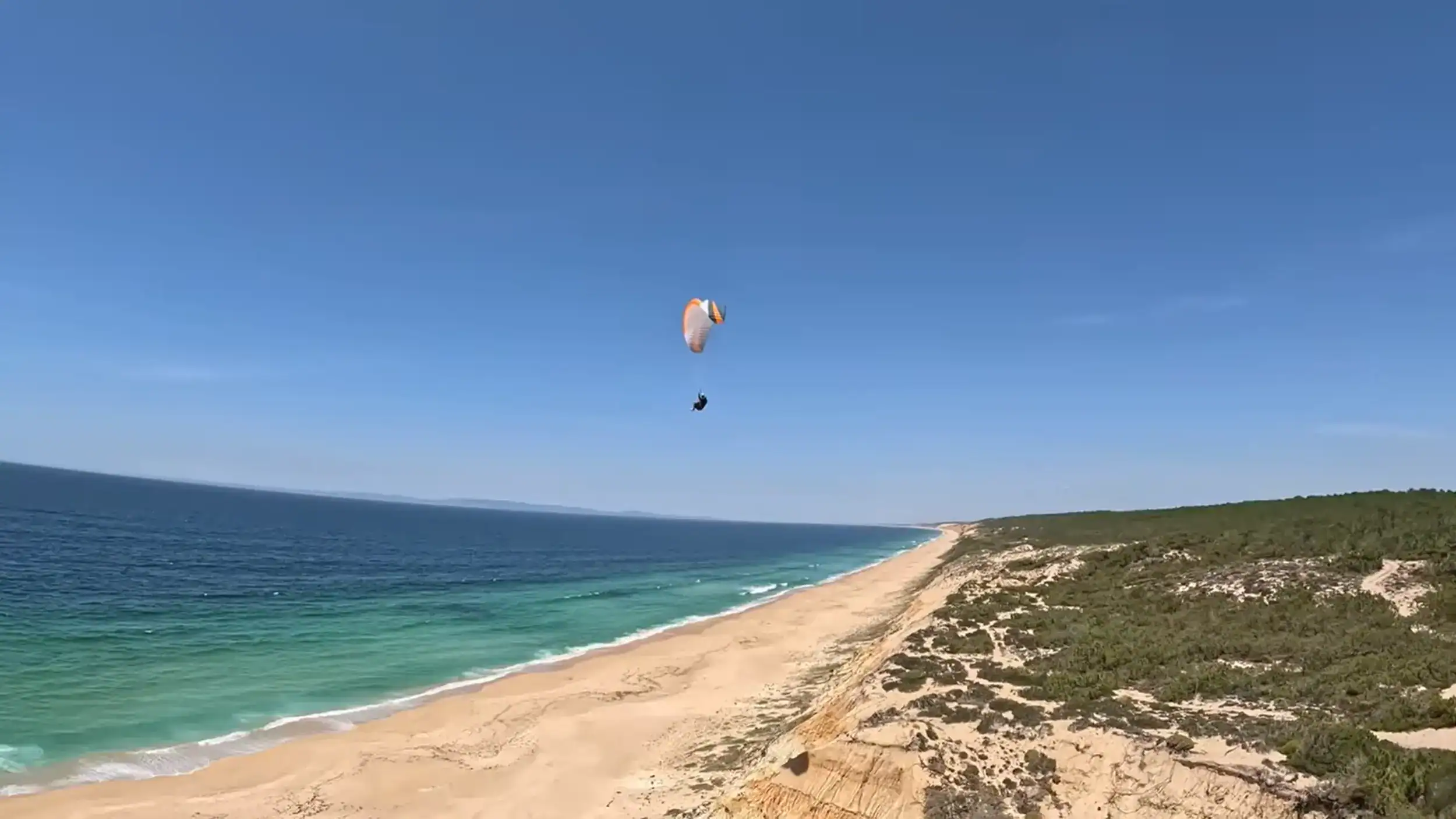 Paraglider soaring over Aberta Nova beach with turquoise Atlantic waters below
