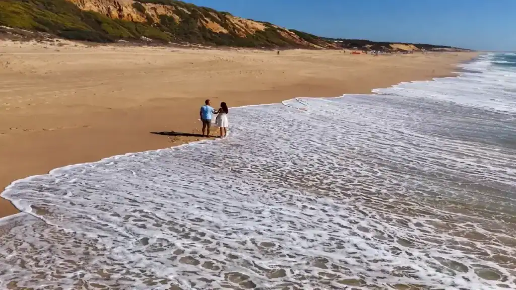 Couple walking hand in hand along a wide empty Atlantic shoreline at golden hour