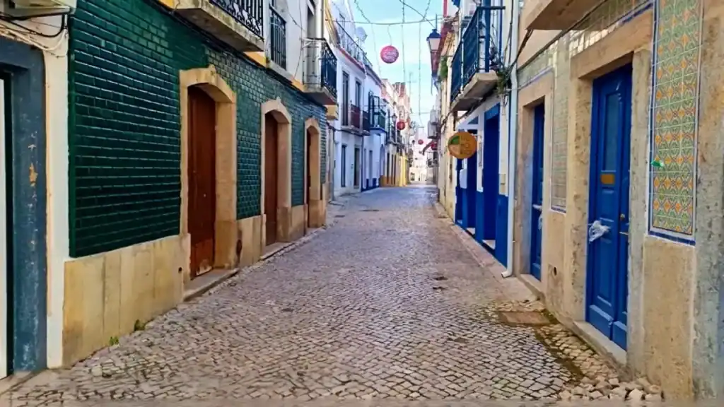 Narrow cobblestone lane flanked by tiled facades, blue doors, and wrought iron balconies