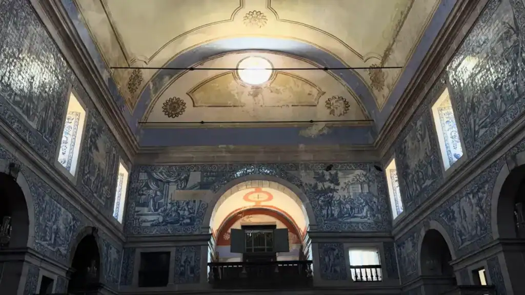 Church interior with floor-to-ceiling blue and white azulejo tile panels beneath a vaulted ceiling