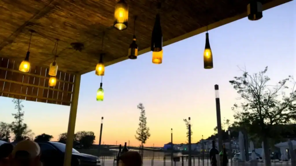 Wine bottle pendant lights hanging from a thatched terrace roof at sunset over the River Sado