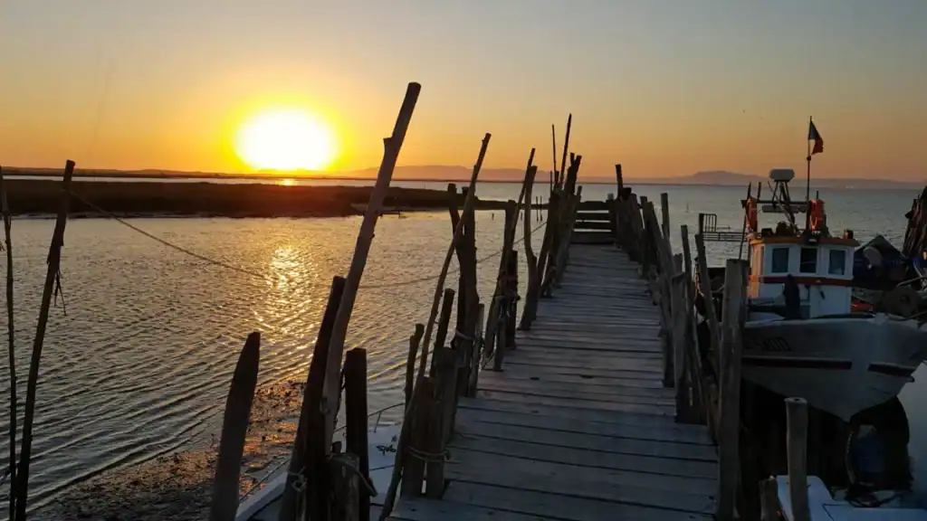 Wooden boardwalk leading toward a deep orange sunset over the Sado Estuary
