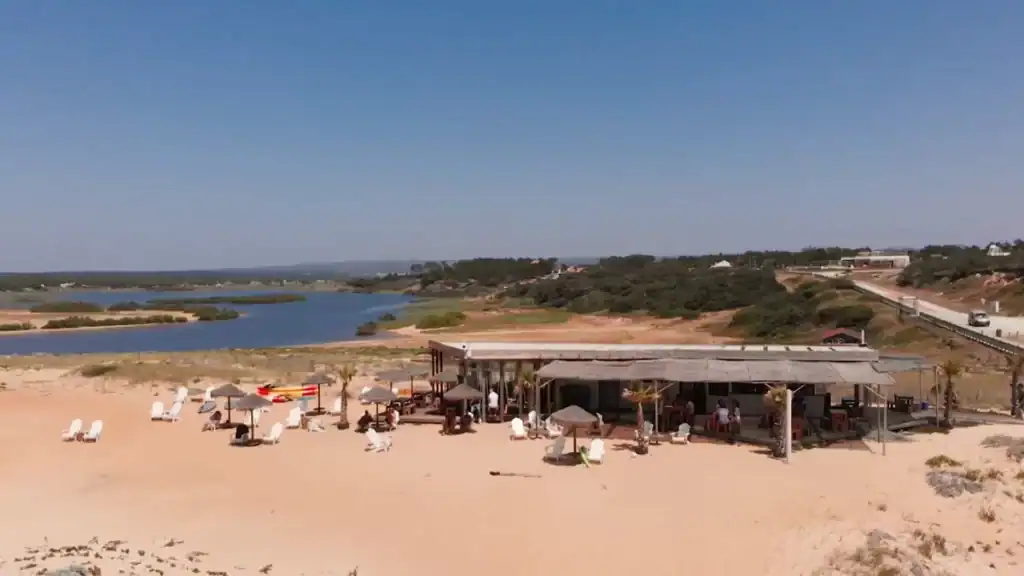Rustic beach bar with straw parasols and white sun loungers where a lagoon meets the sand