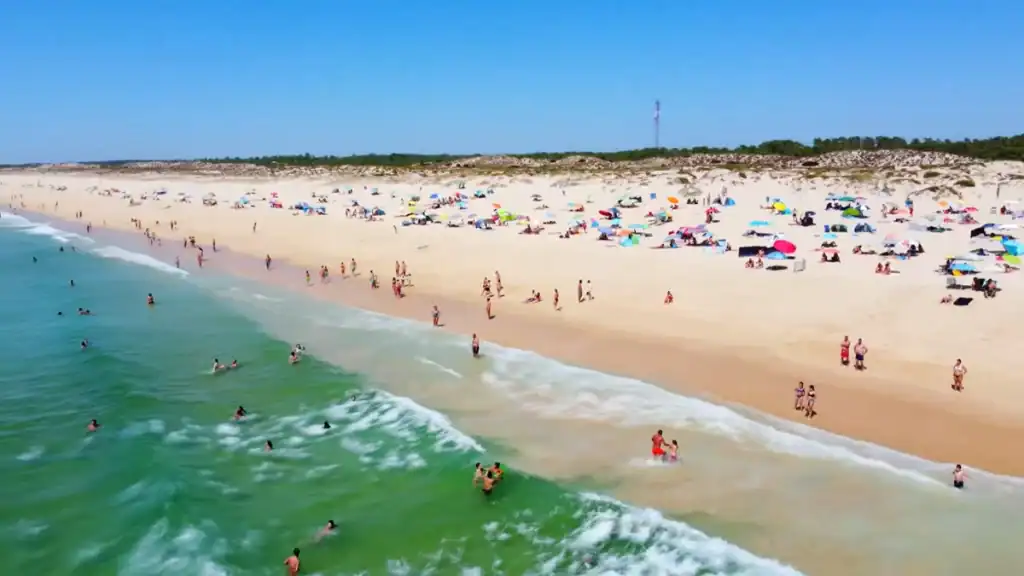Crowded summer beach with turquoise surf and colourful parasols along the Comporta Coast
