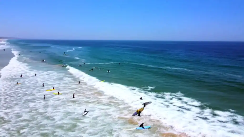 Surfers and bodyboarders scattered across rolling Atlantic waves at a wide open beach