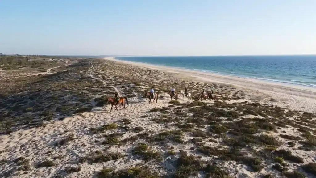 Group of horse riders crossing scrub-covered sand dunes above a deserted Atlantic shoreline