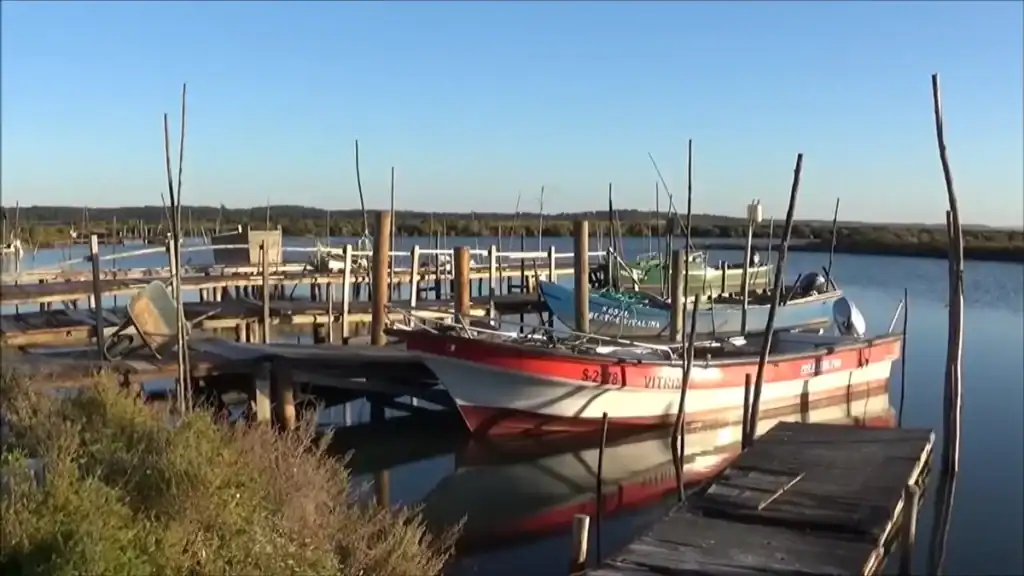 Weathered fishing boats moored at a rustic timber dock on calm estuary waters