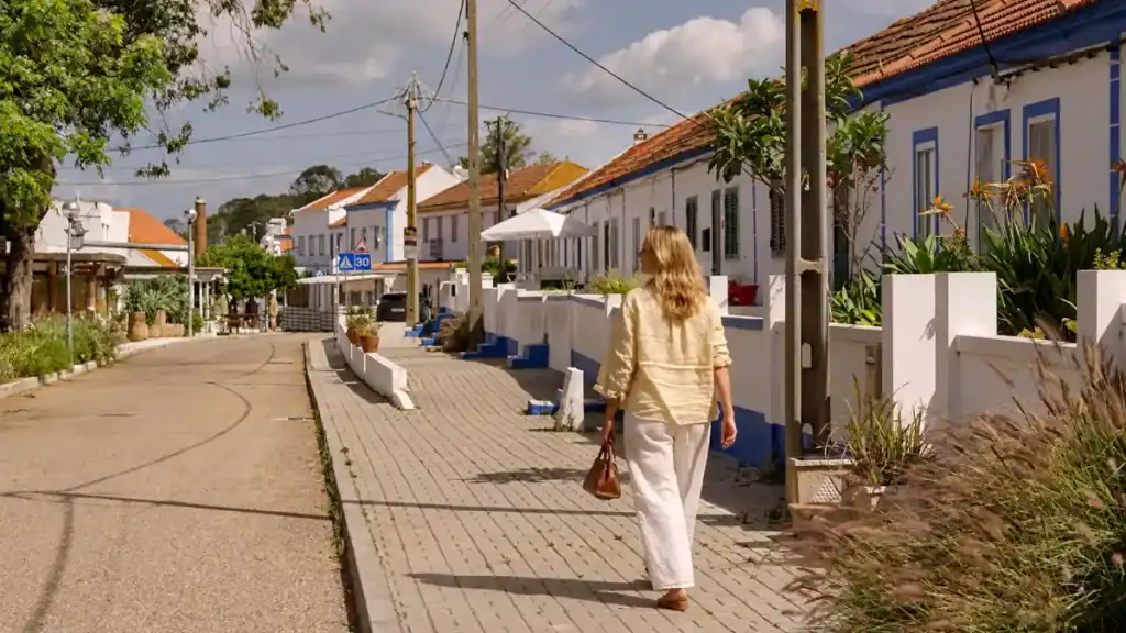 Woman walking past whitewashed houses with blue trim in Comporta village, Portugal