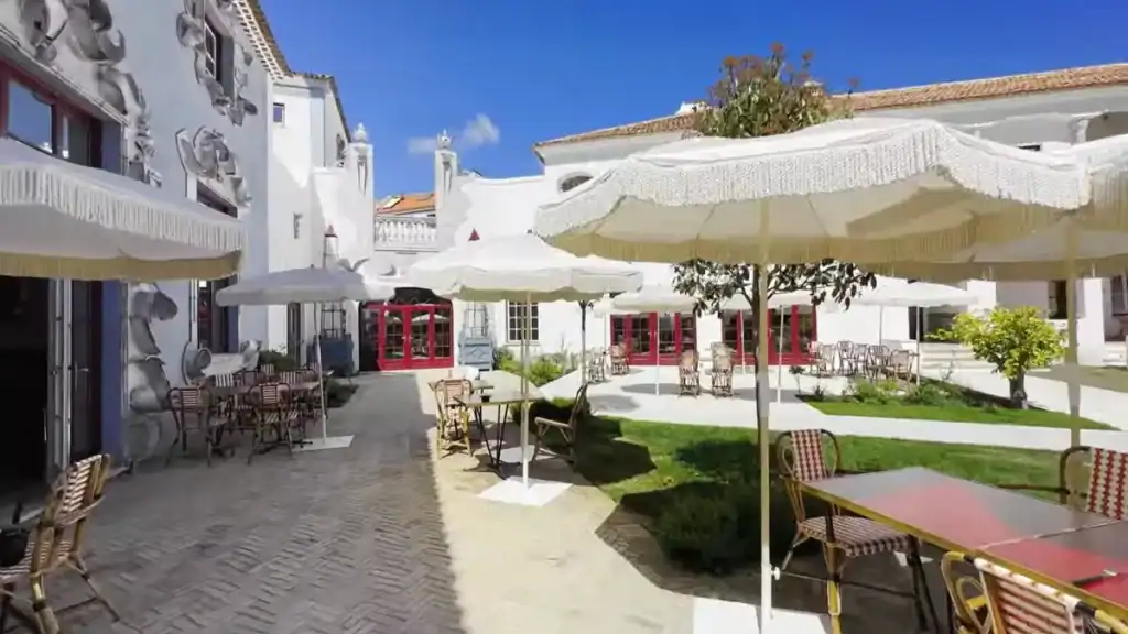 Whitewashed hotel courtyard with fringed parasols, red-framed windows and sculptural facade details