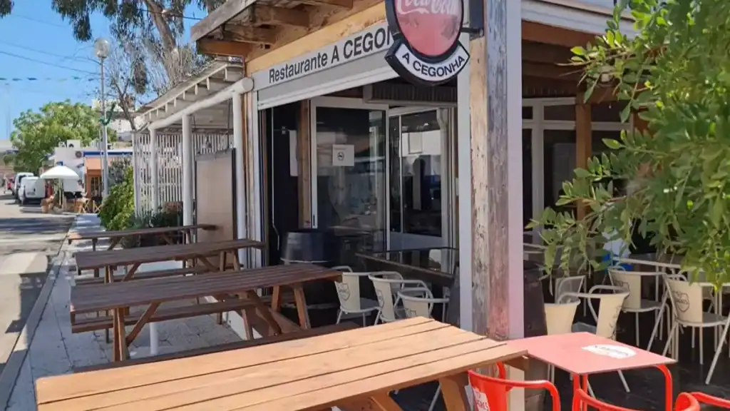 Outdoor terrace of Restaurante A Cegonha with wooden benches on a quiet village street