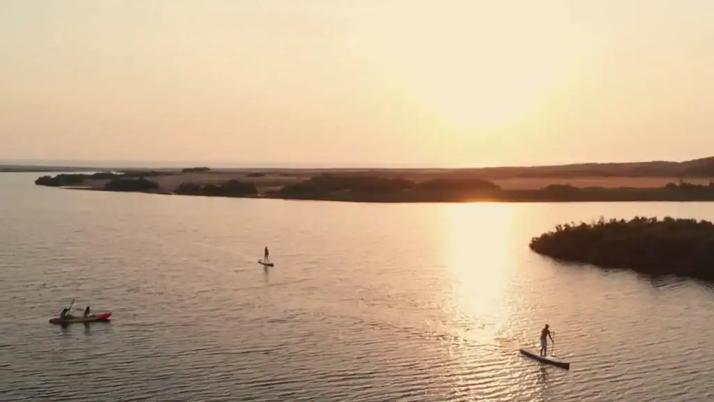 Two paddleboarders and a kayak on a calm lagoon at sunset with golden light reflecting on the water