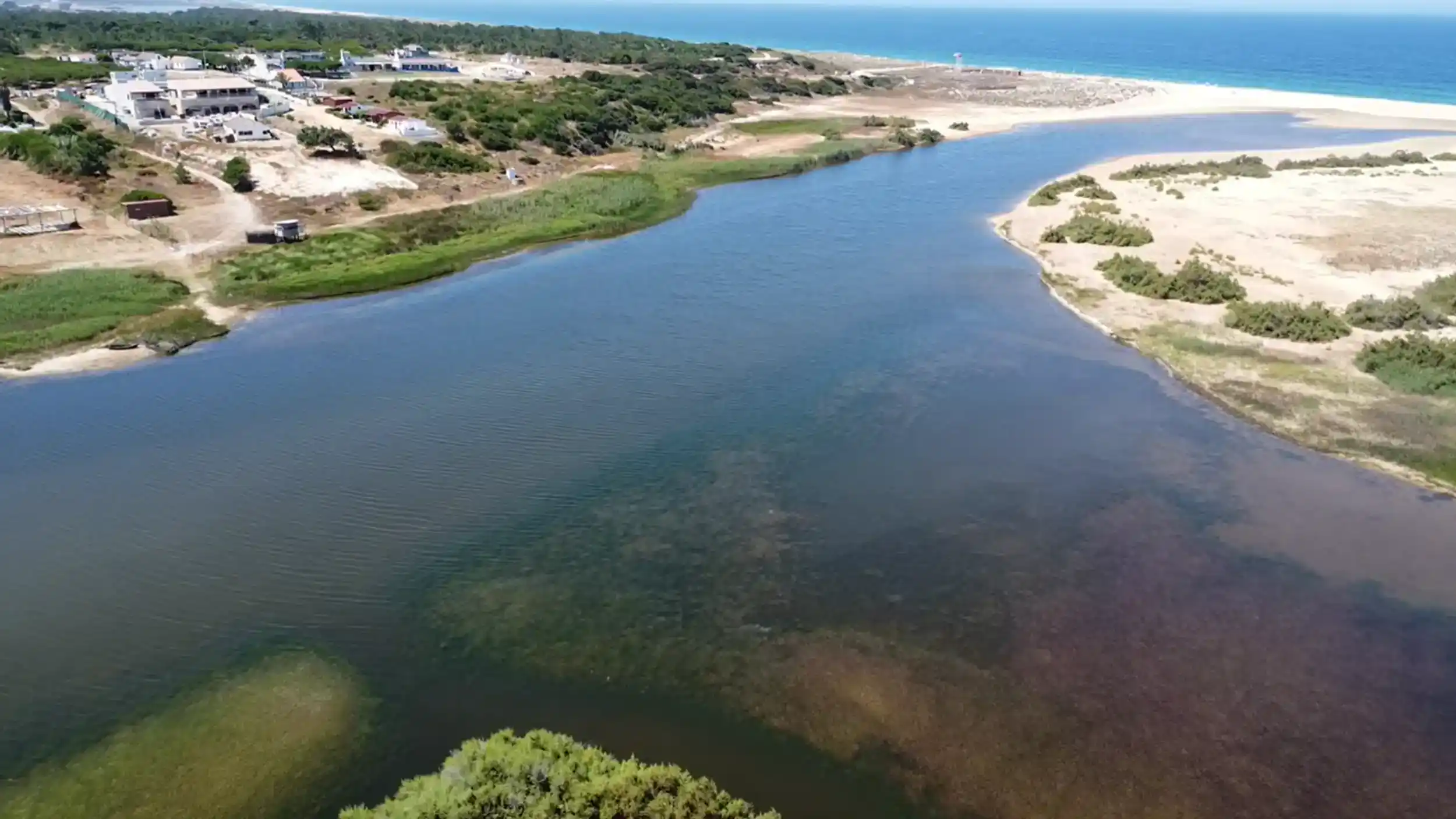 Lagoon channel meeting Atlantic beach at Melides with sandy dunes and pine forest beyond
