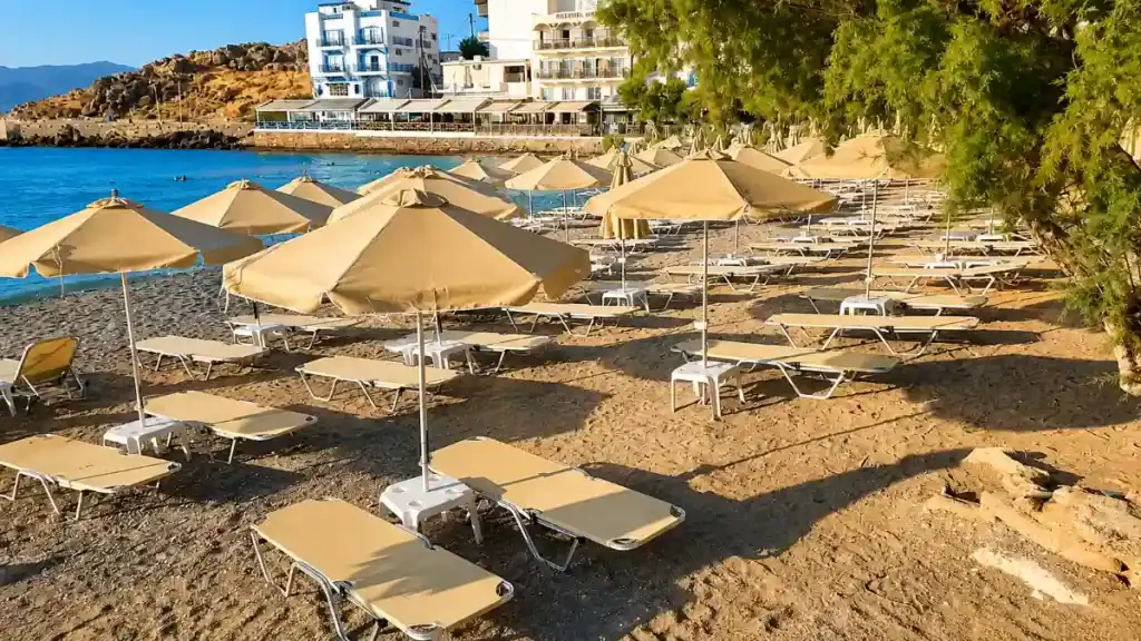 Rows of beige umbrellas and sunbeds lining Ammoudi Beach in the morning
