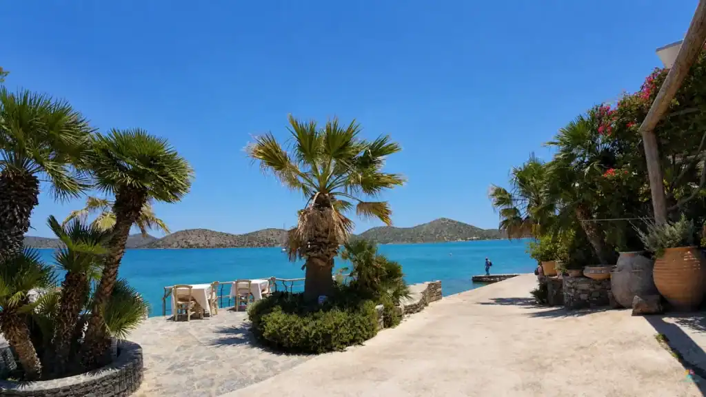 Palm-lined seafront promenade with taverna tables facing Mirabello Bay in Elounda.